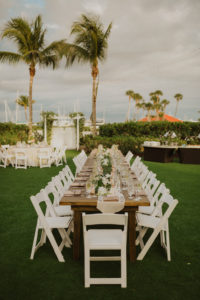Outdoor Garden Waterfront Wedding Reception with Tropical Wedding Decor, Long Feasting Wooden Tables with Burlap Runners, White Folding Chairs, Against Palm Tree Background | Sarasota Beachfront Wedding Venue Longboat Key Club