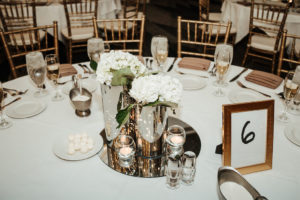 Classic White Wedding Reception Decor with Low Floral Centerpieces in Silver Vases and Round Mirror Tray, Gold Chiavari Chairs | Rentals A Chair Affair