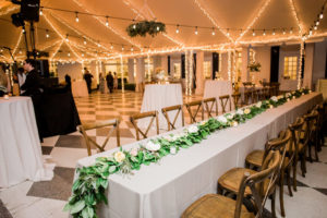 Boho Modern Chic Tent Wedding Reception Decor, Long Feasting Table with Greenery Garland and White, Yellow and Blush Pink Roses, Wooden Crossback Chairs and Tall Cocktail Tables, String Lights | Wedding Venue Tampa Yacht and Country Club