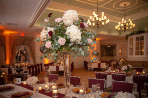 FSU Inspired Elegant Wedding Decor, Tall Floral Centerpiece with White Hydrangeas, Blush Pink Roses and Red Carnations with Silver Dollar Eucalyptus Greenery, Silver Chiavari Chairs with Burgundy Linens, Gold Charges, On Long Feasting Table | Brooksville Golf Course Southern Hills Plantation