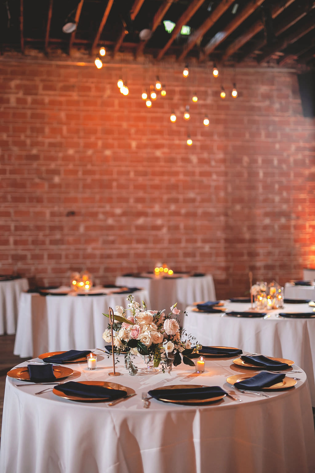 Classic Indoor Reception and Wedding Decor with Round Tables with White Linens, Navy Blue Napkins Low Floral Centerpieces, Ivory, Blush Pink, Flowers with Greenery, Gold Chargers | Tampa Bay Wedding Venue NOVA 535