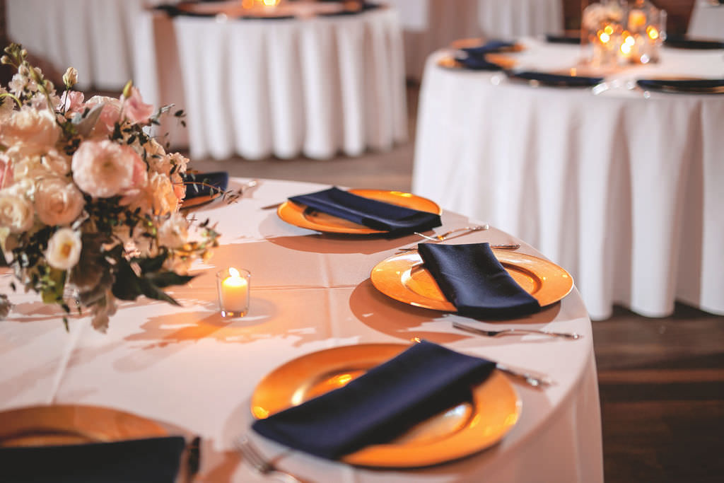 Classic Indoor Reception and Wedding Decor with Round Tables with White Linens, Navy Blue Napkins Low Floral Centerpieces, Ivory, Blush Pink, Flowers with Greenery, Gold Chargers
