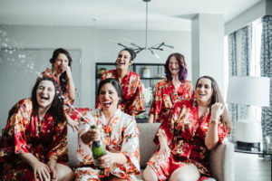 Florida Bride and Bridesmaids Popping Champagne Bottle, Wearing Matching Red Silk Floral Robes | Tampa Bay Boutique Hotel and Wedding Venue The Hotel Alba in Westshore