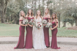 Florida Bridal Party Portrait, Bride in Romantic White Calle Blanch Wedding Dress, Bridesmaids in Long Burgundy Bill Levkoff Dresses with Off The Shoulder Sleeves, Carrying Red, Blush Pink, and White Floral Bridal Bouquets with Silver Dollar Eucalyptus Greenery | Tampa Bay Bridal Shop Nikki’s Glitz and Glam Boutique