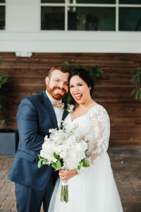 Classic, Elegant Florida Bride and Groom Wedding Portrait, Bride in Lace Illusion Sleeve Wedding Dress, Carrying Traditional Round White Floral Bouquet with Greenery, Groom in Navy Suit and Champagne Bowtie | Tampa Bay Boutique Hotel and Wedding Venue The Hotel Alba in Westshore