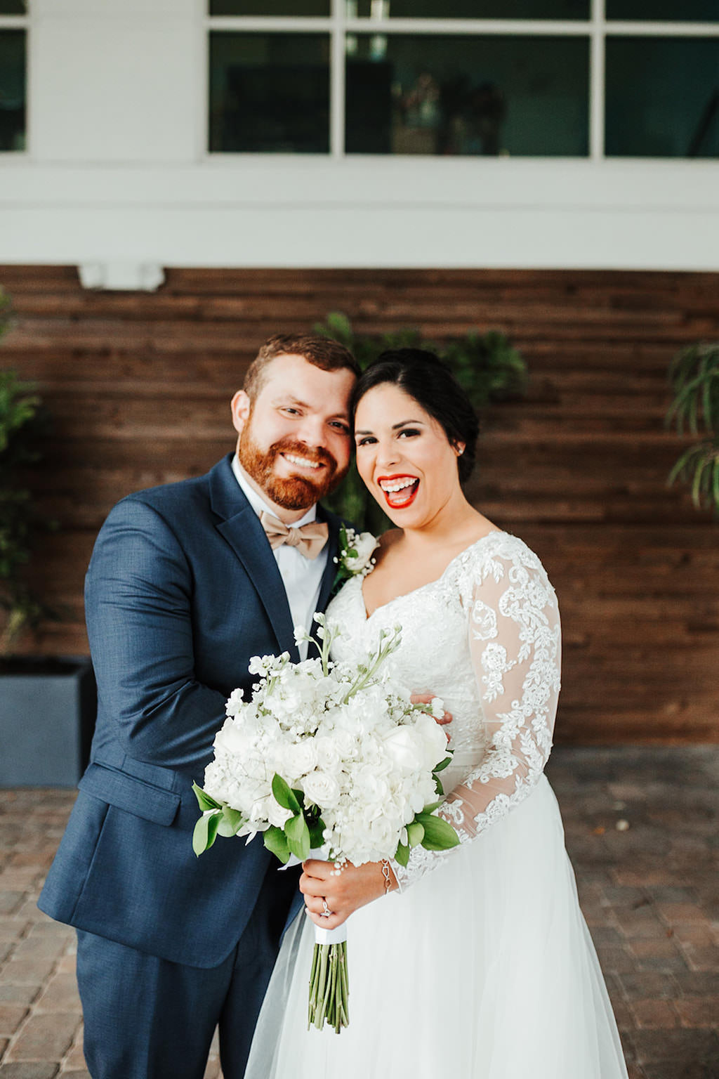 Classic, Elegant Florida Bride and Groom Wedding Portrait, Bride in Lace Illusion Sleeve Wedding Dress, Carrying Traditional Round White Floral Bouquet with Greenery, Groom in Navy Suit and Champagne Bowtie | Tampa Bay Boutique Hotel and Wedding Venue The Hotel Alba in Westshore