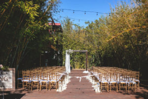 Romantic Downtown St. Pete Bamboo Garden Ceremony with String Lights, Wooden Arch and Floral Wedding Decor, White Hanging Linens, Chiavari Chairs, White Flower Petals Lining the Aisle | Tampa Bay Unique Historic Wedding Venue NOVA 535