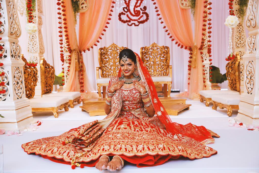 Elegant Extravagant Traditional Indian Bride in Gold and Red Sari and Veil with Henna Tattoo and Elegant Bridal Accessories, Gold Chairs, Peach, Coral Linen Draping, Blush Pink Linen Backdrop, Red and Gold Decorative Elements | Tampa Wedding Hair and Makeup Michele Renee the Studio