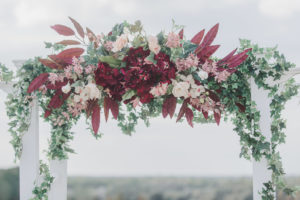 Romantic FSU Inspired Wedding Decor, Burgundy, Blush Pink, and White Floral Arrangement on Top of White Wedding Arch with Greenery and Garland