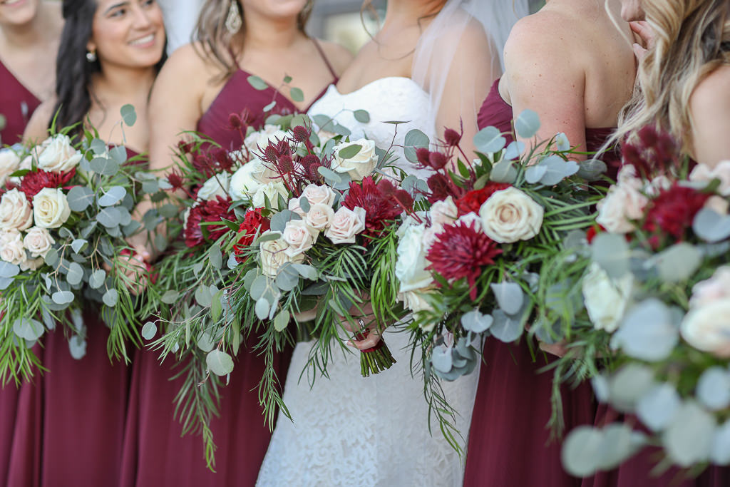 Bride and Bridesmaids in Long Burgundy Wine Red Dresses Holding Garden Style Red, Ivory, and Greenery Floral Bouquets | Tampa Bay Wedding Photographer Lifelong Photography Studios | Tampa Bay Wedding Planner Breezin' Weddings