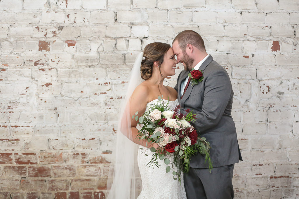 Tampa Bay Groom and Bride in Strapless Lace Fitted Wedding Dress and Cathedral Length Veil with Organic Red, Blush, Ivory and Greenery Floral Bouquet and White Brick Backdrop | Tampa Wedding Photographer Lifelong Photography Studios | Industrial Historic Wedding Venue Rialto Theatre | Tampa Wedding Hair and Makeup Artists Michele Renee the Studio
