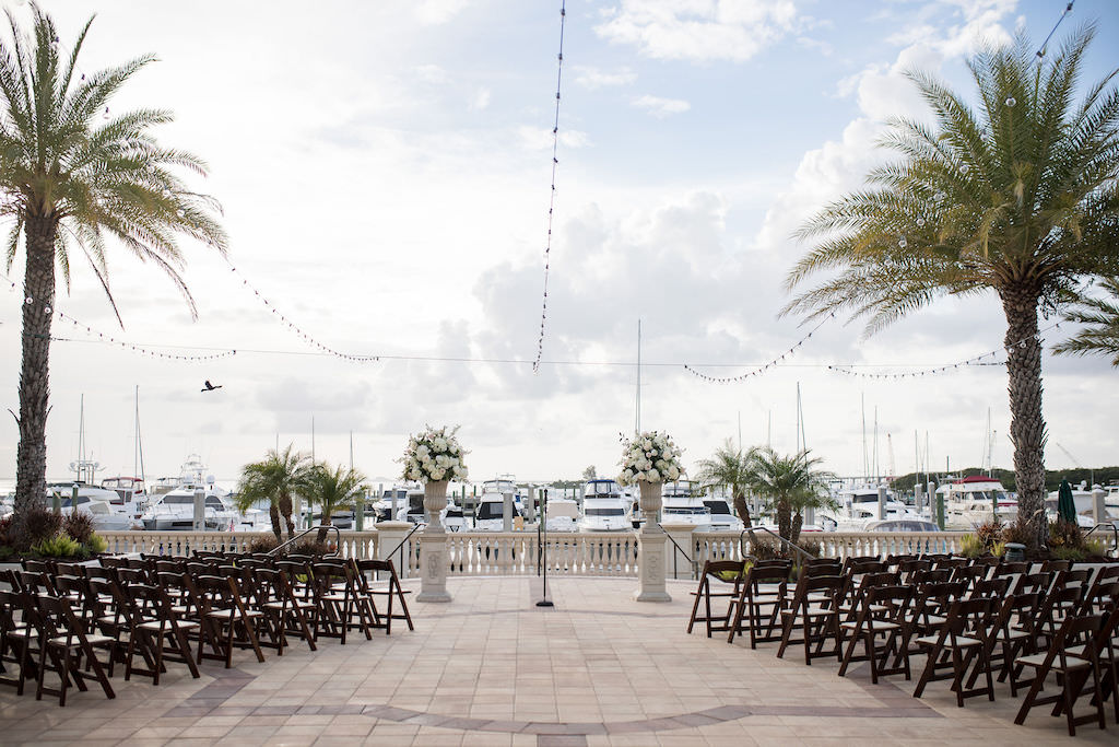 Outdoor Waterfront Classic Elegant Wedding Ceremony Decor, Tall Pedestals with White Floral Bouquets, String Lights and Wooden Folding Chairs | Tampa Bay Wedding Venue Westshore Yacht Club | South Tampa Luxury Wedding Planner NK Productions Wedding Planning