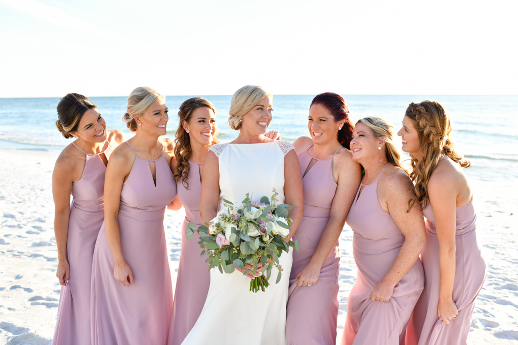 Tampa Bay Bride in White Fitted High Neckline Cap Sleeve Christina Wu Wedding Dress Holding Garden Organic White, Ivory, Purple and Greenery Floral Bouquet with Bridesmaids in Matching Dusty Rose Dresses on the Beach Wedding Portrait