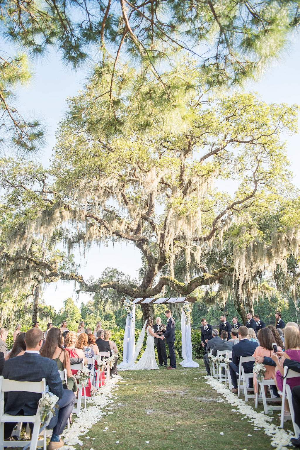 Florida Bride and Groom Exchanging Vows Under Wooden Arch with White Draping and Blue and White Flower Bouquets on Golf Course Wedding Ceremony Portrait | Tampa Bay Wedding Photographer Kristen Marie Photography | Innisbrook Golf & Spa Resort Wedding Venue