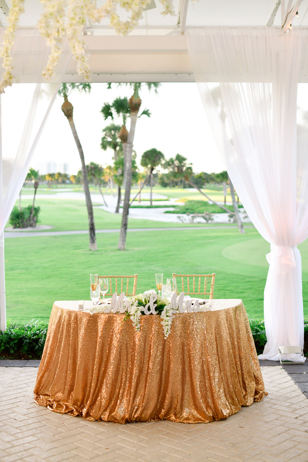 Tropical Classic Elegant Wedding Reception Decor, Sweetheart Table with Sparkle Gold Linen, White and Greenery Floral Arrangement and Gold Chiavari Chairs with White Sheer Draping and Golf Course Backdrop | Sarasota Wedding Venue The Resort at Longboat Key Club