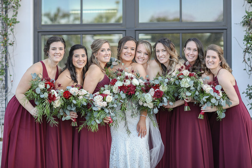 Bride and Bridesmaids in Long Burgundy Wine Red Dresses Holding Garden Style Red, Ivory, and Greenery Floral Bouquets | Tampa Bay Wedding Photographer Lifelong Photography Studios | Tampa Bay Wedding Planner Breezin' Weddings | Tampa Bay Hair and Makeup Team Michele Renee the Studio