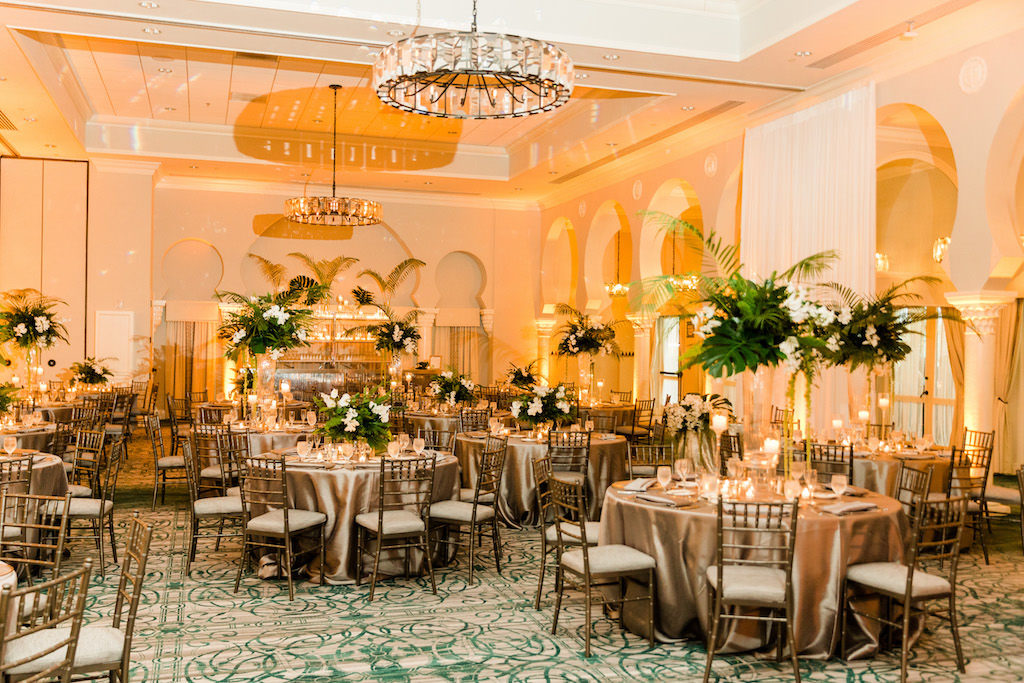 Tropical Florida Inspired Wedding Reception, Modern Wedding Decor, Tall Floral Centerpieces with Green Monstera Leaves, Large Palm Fronds, White Orchids, Round Tables with Silver Linens, Chiavari Chairs, Grand Ballroom of The Vinoy Renaissance St. Petersburg Resort & Golf Club | Over the Top Rental Linens | Tampa Bay Florist Bruce Wayne Florals | Florida Luxury Wedding Planner Parties A'La Carte