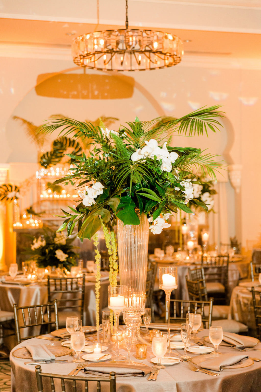 Tropical Inspired, Modern Wedding Reception Decor, Tall Centerpieces with Green Monstera Leaves, Large Palm Fronds, White Orchid Florals, Hanging Green Amaranthus, Round Tables with Silver Linens, Chiavari Chairs, Grand Ballroom of The Vinoy Renaissance St. Petersburg Resort & Golf Club | Over the Top Rental Linens | Tampa Bay Florist Bruce Wayne Florals | Florida Luxury Wedding Planner Parties A'La Carte