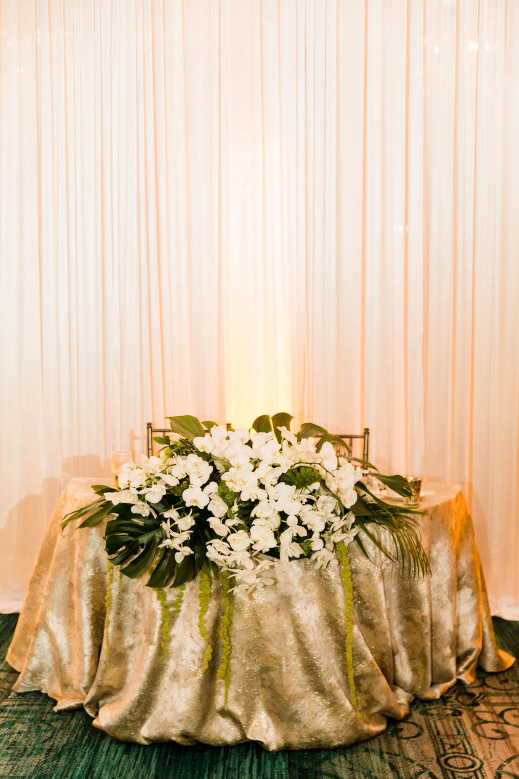 Tropical Inspired, Modern Wedding Reception Decor, Silver Accented Sweetheart Table with Green Monstera Leaves and Lush Cascading White Orchid Florals | Over the Top Rental Linens | Tampa Bay Florist Bruce Wayne Florals | Florida Luxury Wedding Planner Parties A'La Carte