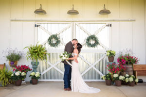 Tampa Bay Bride and Groom Kissing Outside White and Metal Barn Doors, Bride Holding Greenery and White, Ivory Floral Bouquet | Rustic Wedding Venue Covington Farm