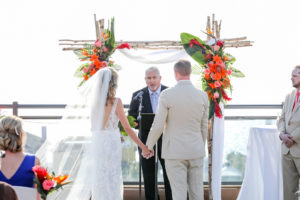 Florida Bride and Groom at Tropical, Beach Inspired Rooftop Waterfront Wedding Ceremony, Gold and Coral Wedding Decor, White Folding Chairs with Bright Flowers in Bouquets, Island Inspired Arch with Vibrant Floral Arrangements | Boutique St. Pete Beach Wedding Venue Hotel Zamora | Tampa Bay Wedding Photographer Lifelong Photography Studios