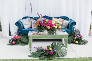 Modern, Tropical Garden Inspired Wedding Decor, Blue Velvet Lounge Seating and Couch, Dusty Rose Gold and Silver Accent Pillows, Mirrored Table, Whimsical Pink, Yellow, Orange, Purple Floral Centerpiece with Green Monstera Leaves, Against White Draping | Tampa Bay Wedding Planner Special Moments Event Planning | Tampa Bay Wedding Florist and Rentals Gabro Event Services