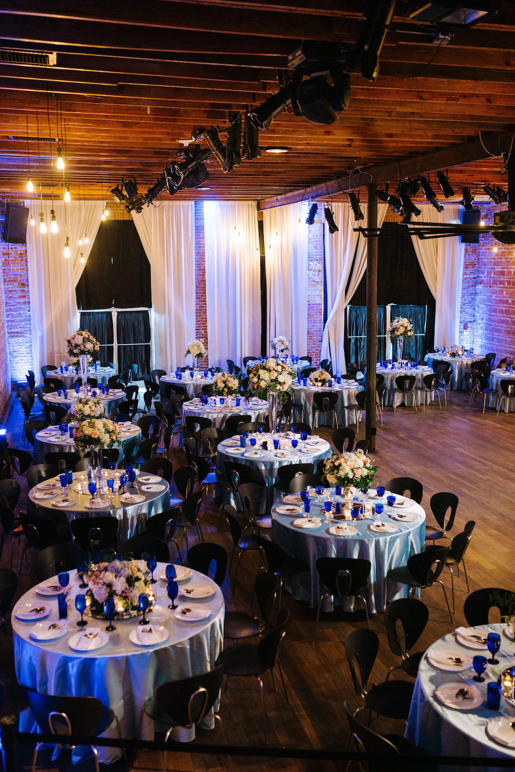 Modern, Romantic Reception and Florida Wedding Decor, Tall Floral Centerpieces with White, Peach, Pink, Ivory Flowers, Round Tables with Silver Tablecloths, Blue Stemware, Exposed Brick Wall | Tampa Bay Premier Wedding Venue NOVA 535 in Downtown St. Pete