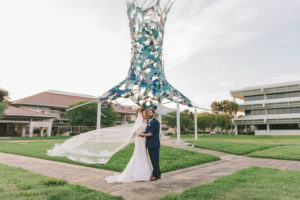 Creative Florida Bride and Groom Wedding Portrait with Bride's Cathedral Length Veil Blowing in Wind Outside with Art Sculpture | Wedding Photographer Kera Photography | St. Pete Wedding Venue The Poynter Institute