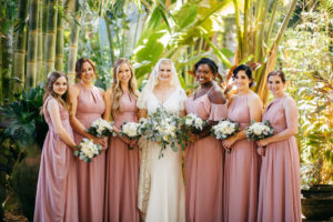 Tampa Bay Bride in V Neckline Simple Classic with Sleeves Wedding Dress and Lace Veil Holding Organic Greenery and Ivory Floral Bouquet, Bridesmaids in Mauve Pink Dresses Holding White Flower Bouquets | Tampa Bay Wedding Hair and Makeup Femme Akoi