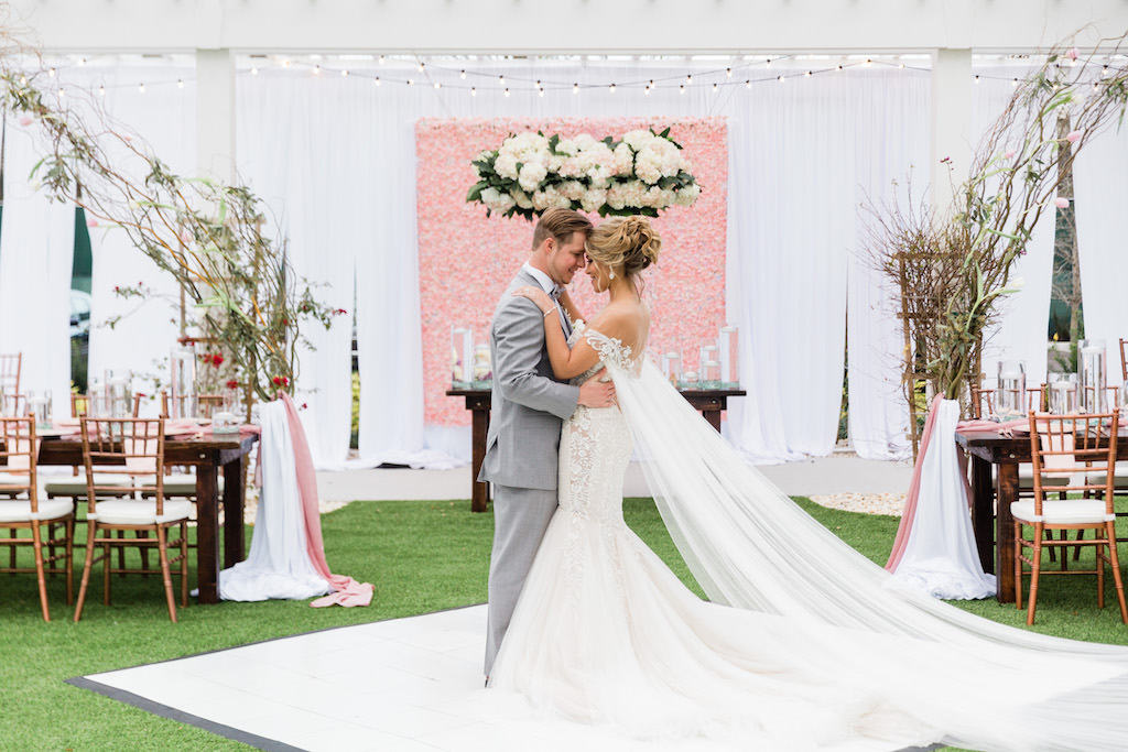 Modern Florida Bride and Groom on Dance Floor, Wearing Wearing White Mermaid Style Illusion Lace Couture Wedding Dress with Long Tulle Cape, Whimsical Garden Wedding Decor and Reception under Gazebo, Pink Floral Boxwood Wall, White Draping, Hanging Floral Arrangement, Long Feasting Tables. Rose Gold Chiavari Chairs, Floral Curly Willow Arches, Sweetheart Table with Ghost Acrylic Chairs, Outdoor Dance floor | Tampa Bay Wedding Planner Special Moments Event Planning | Tampa Bay Wedding Florist Gabro Event Services | Tampa Bay Wedding Rentals A Chair Affair | Tampa Bay Hair and Makeup Artists Femme Akoi | Tampa Bay Couture Wedding Dress Boutique Isabel O'Neil Bridal Collection |