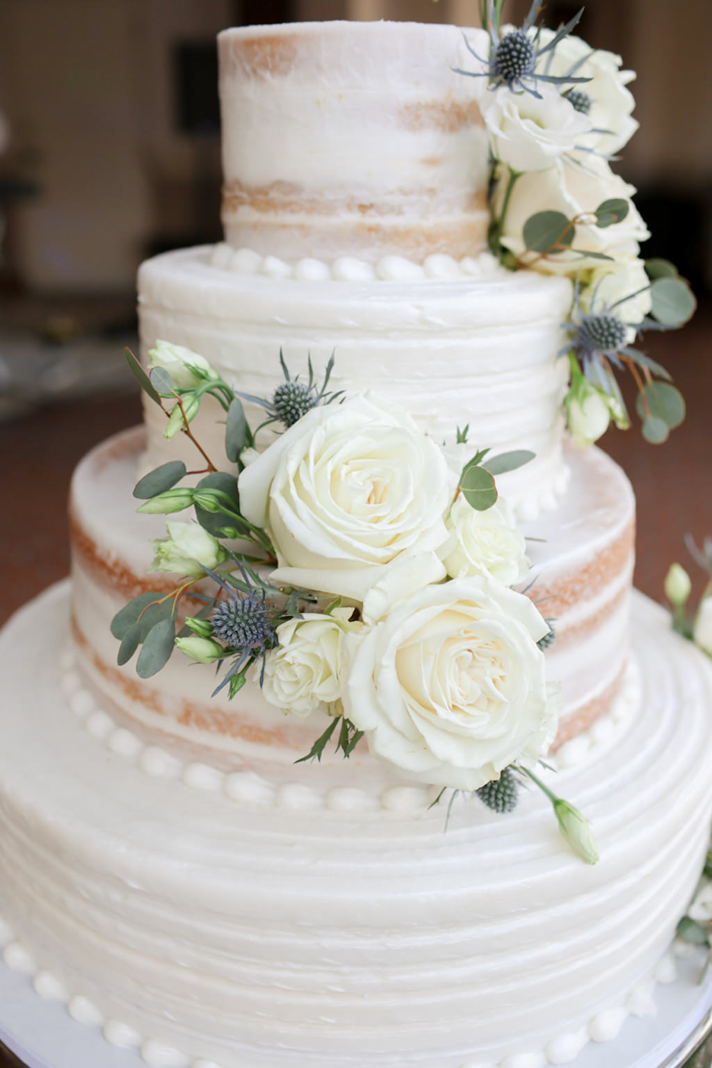 Rustic Elegant Four Tier White and Semi Naked Wedding Cake with Ivory Roses and Blue Thistle. Real Flowers | Wedding Photographer Lifelong Photography Studios