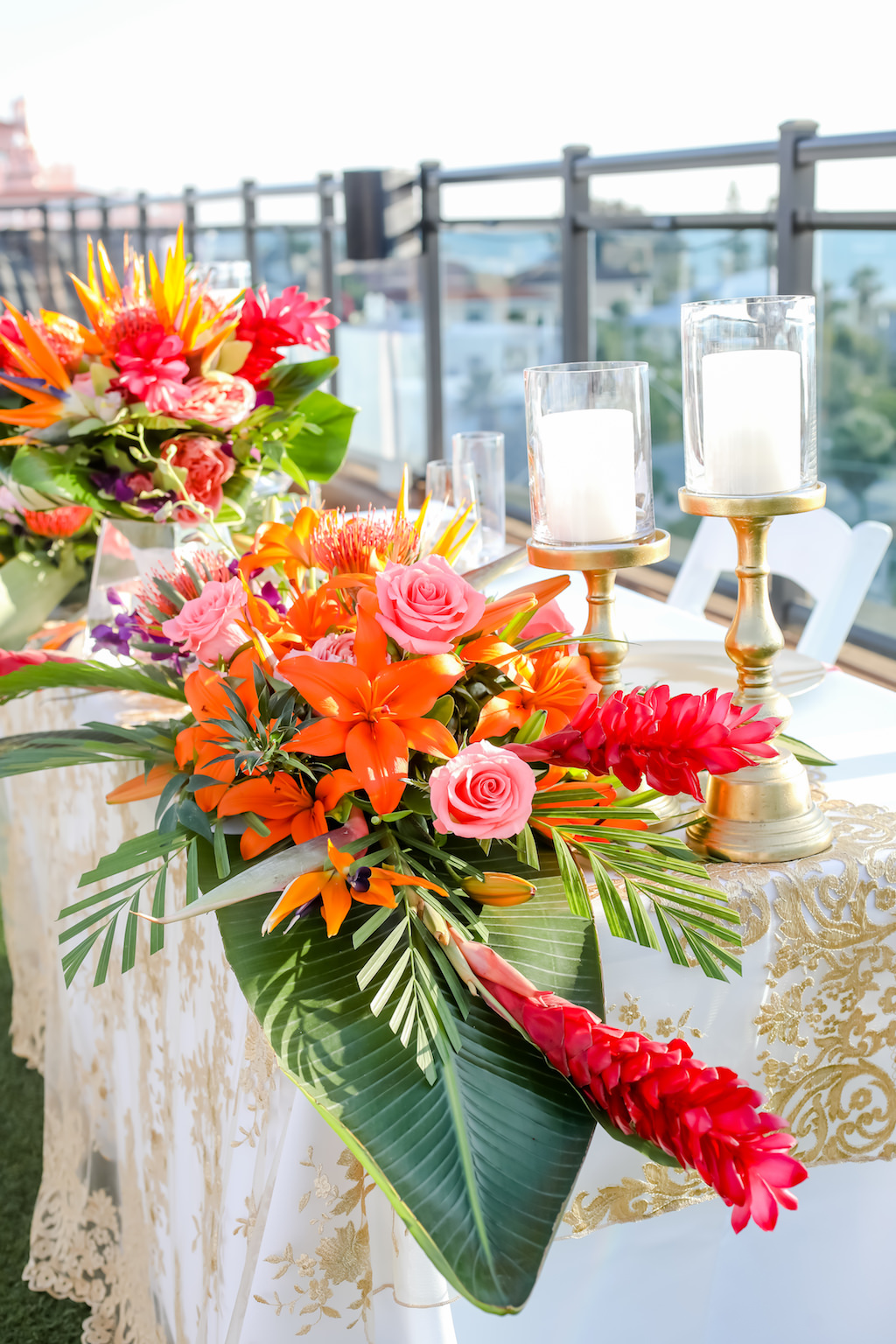Tropical, Florida Beach Inspired Floral Arrangement for Sweetheart Table, White Tablecloth and Sheer Gold Lace Overlay, Vibrant Orange, Pink, Coral, Yellow, and Greenery Centerpiece, Rooftop Waterfront Wedding Reception | St. Pete Beach Wedding Venue Hotel Zamora | Tampa Bay Wedding Photographer Lifelong Photography Studios | Tampa Wedding Rentals Gabro Event Services