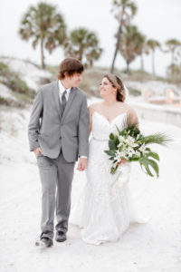 Clearwater Beach Bride and Groom Wedding Portrait, Bride in Fitted Spaghetti Strap Lace V Neckline Wedding Dress with Rhinestone Belt Holding Tropical Monstera Leaf, Areca Leaves and White Orchid Floral Bouquet | Tampa Bay Wedding Photographer Lifelong Photography Studios