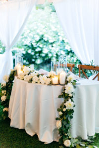 Elegant, Simple, Classic Garden Tent Wedding Reception Decor, Sweetheart Table with White Linen, Wooden Crossback Chairs, Greenery Garland with White and Ivory Florals, Hurricane Glass Candlesticks | Tampa Bay Wedding Rentals Gabro Event Services