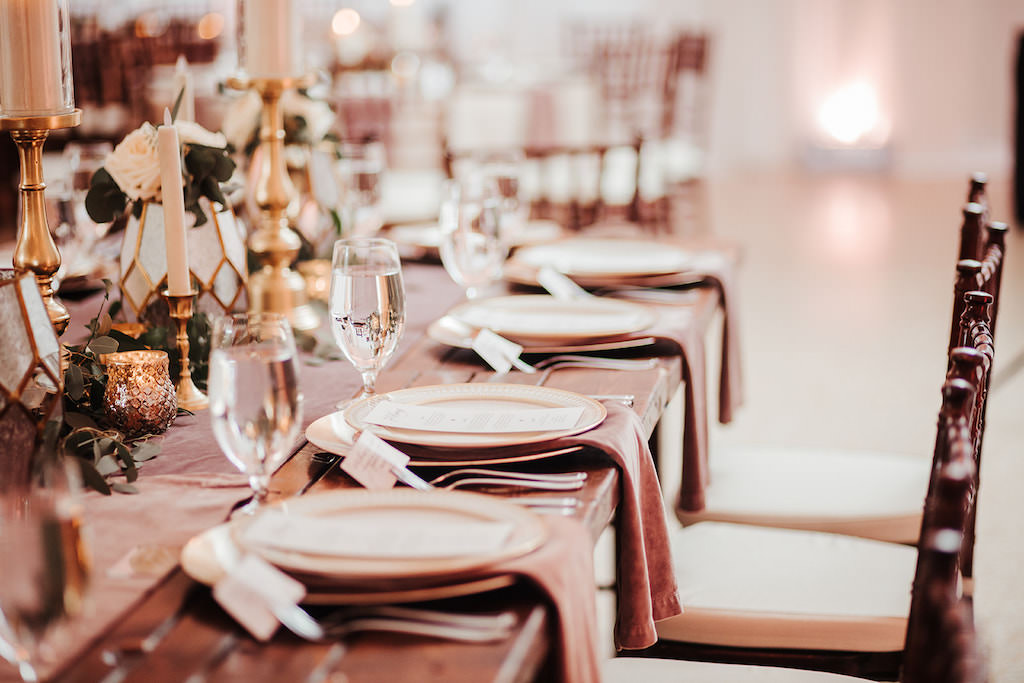 Florida Garden Inspired Wedding Reception Decor on Long Wooden Feasting Table with Mauve Table Runner and Gold Candlesticks, Mahogany Chiavari Chairs | Tampa Bay Wedding Rentals by A Chair Affair