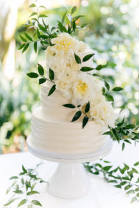 Classic Elegant Three Tier White Wedding Cake Garnished with Real Ivory Flowers and Greenery Leaves on White Cake Stand