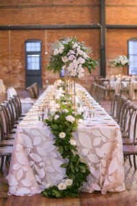Elegant Modern Romantic Tuscan Inspired Wedding Reception Decor, Long Feasting Table with Floral Linen, Greenery and Ivory Floral Garland, Tall Gold Stand with Ivory White and Greenery Floral Centerpiece | Tampa Bay Wedding Photographer Carrie Wildes Photography | Tampa Bay Wedding and Event Rentals by Kate Ryan Event Rentals | Industrial Tampa Wedding Venue Armature Works | Over The Top Linens