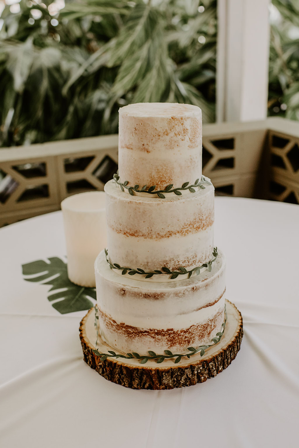 Three Tier Rustic White Semi Naked Wedding Cake Garnished with Greenery on Round Wood Platter
