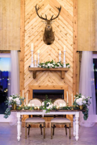Rustic Country Chic Wedding Reception Decor, White Wooden Sweetheart Table with Greenery and White, Ivory Floral Centerpieces, Candlesticks, Vintage Ivory Cushioned Chairs, Deer Head Mounted on Wall and White Candlesticks | Tampa Bay Luxury Wedding Planner Parties A'La Carte | Tampa Wedding Florist Bruce Wayne Florals