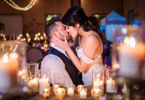 Intimate Romantic Bride and Groom Kissing Portrait with Candle Lit Decor and Hurricane Vases