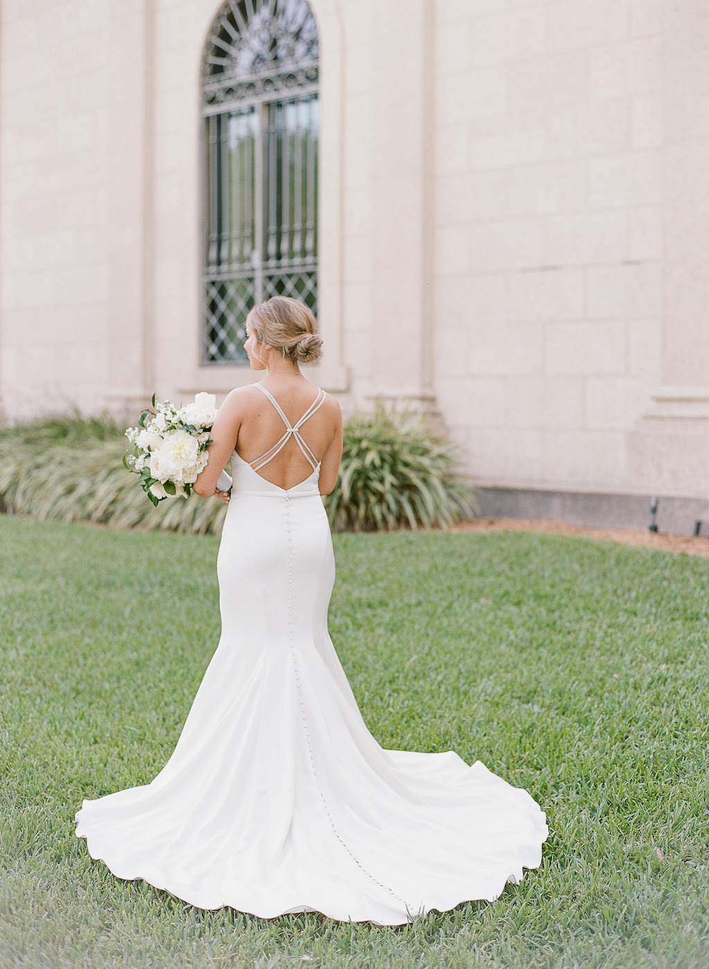 Tampa Bay Bride in Classy Fitted Open Back with Rhinestone Straps and Buttons Wedding Dress Holding White, Ivory, Blush Pink Roses and Greenery Floral Bouquet