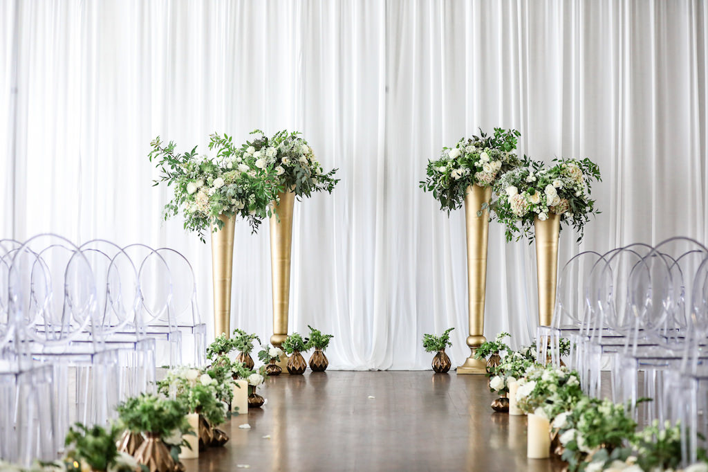 Classic Neutral Wedding Ceremony Decor, Acrylic Clear Ghost Chairs, Small Gold Vases with Greenery and White, Ivory Florals Lining Aisle, Tall Gold Vases with Greenery and Ivory Floral Arrangements | Tampa Bay Wedding Photographer Lifelong Photography Studio | Wedding Rentals Kate Ryan Event Rentals
