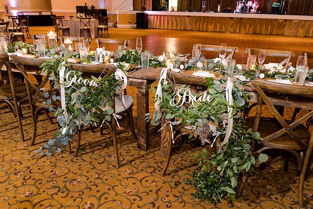 Rustic Elegant Wedding Reception Decor, Long Wooden Feasting Table, Wooden Crossback Chairs, Greenery Garland, Greenery Wreath Accents with Bride and Groom Signs on Chair | Tampa Wedding Venue Innisbrook Golf and Spa Resort