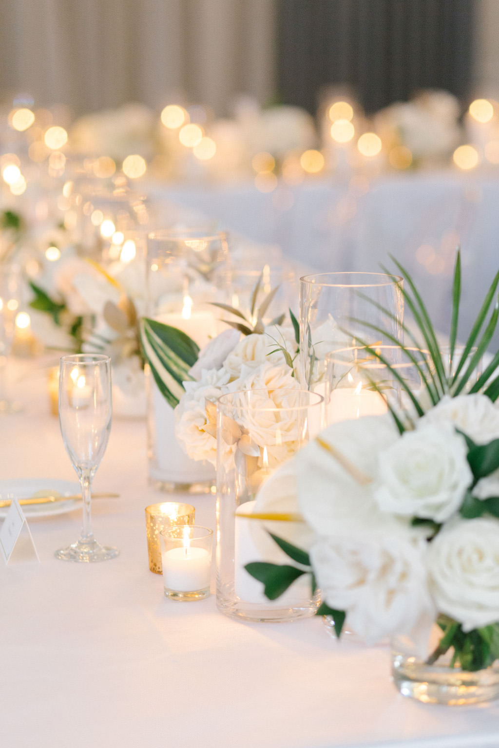 Elegant Modern Wedding Reception Decor, Long Feasting Table with White Linen, White and Tropical Leaf Small Centerpiece Floral Arrangements and Candles | Tampa Bay Wedding Florist Bruce Wayne Florals | Wedding Planner Parties A'La Carte