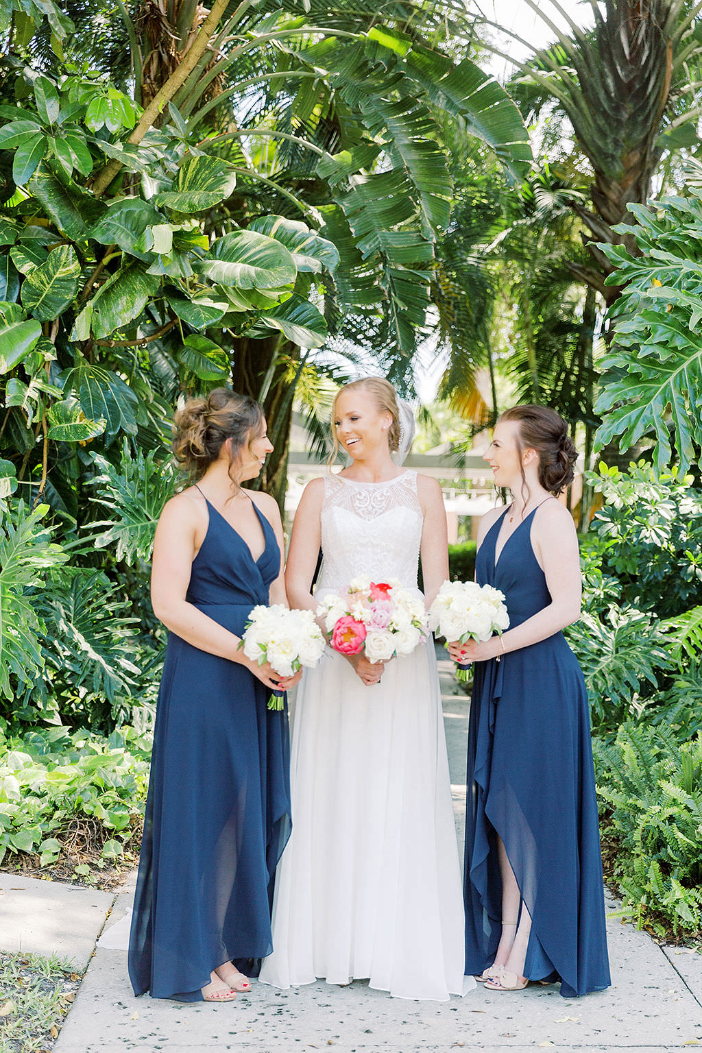 Tampa Bay Bride Wedding Portrait in Tropical Garden in High Illusion and Lace Crew Neck Neckline Wedding Dress with Colorful Pink and White Floral Bridal Bouquet with Bridesmaids in Navy Blue Matching Floor Length Jenny Yang Dresses Holding Ivory Flower Bouquets