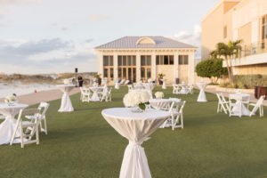 Classic Elegant Wedding Lawn Cocktail Decor, High Low Tables, White Linens, White Folding Chairs, Low White Hydrangea Floral Centerpieces | Tampa Bay Wedding Photographer Kristen Marie Photography | Clearwater Beach Waterfront Wedding Venue Sandpearl Resort | Wedding Florist, Linens and Rentals Gabro Event Services | Wedding Day of Coordinator Special Moments Event Planning