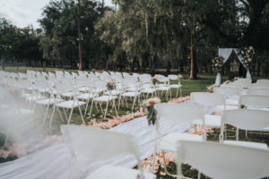 Rustic Chic Wedding Ceremony Outdoor Decor, White Folding Chairs with Blush Pink and White Floral Arrangements, Flower Petal and White Linen Aisle Runner, Linen Draping Arch with Floral Arrangements | Tampa Wedding Venue Rafter J Ranch | Wedding Planner Kelly Kennedy Weddings and Events
