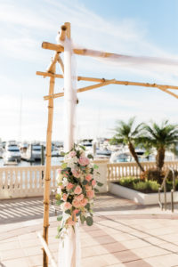 Elegant Florida Waterfront Wedding Ceremony Decor, Bamboo Ceremony Alter, White Linen Drapery, and Pastel Blush Pink, White and Greenery Floral Arrangement