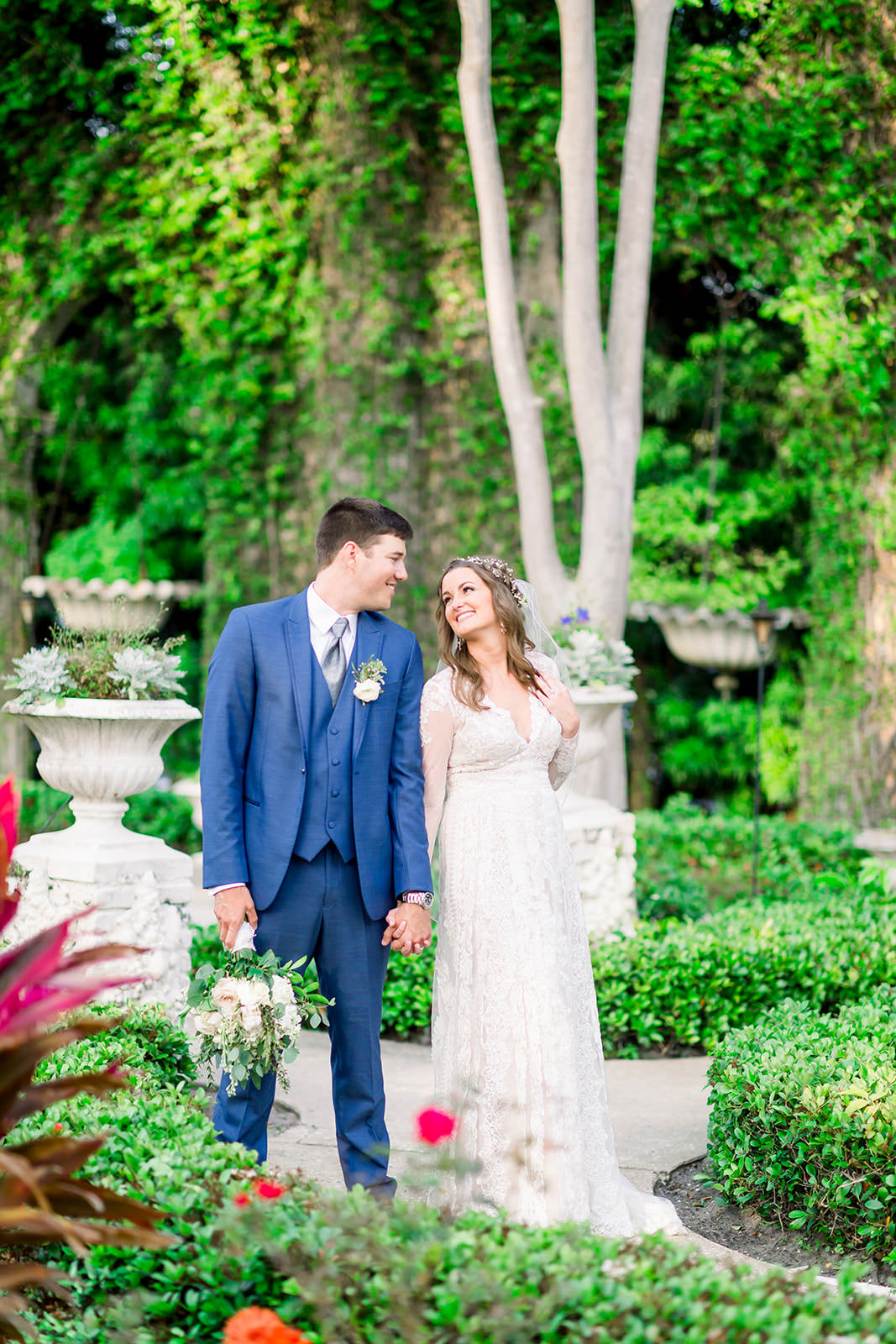 Boho Inspired Florida Bride and Groom in Outdoor Garden Courtyard, Groom in Navy Suit, Bride Holding White Floral Bouquet with Greenery Wedding Portrait | Tampa Bay Wedding Photographers Shauna and Jordon Photography