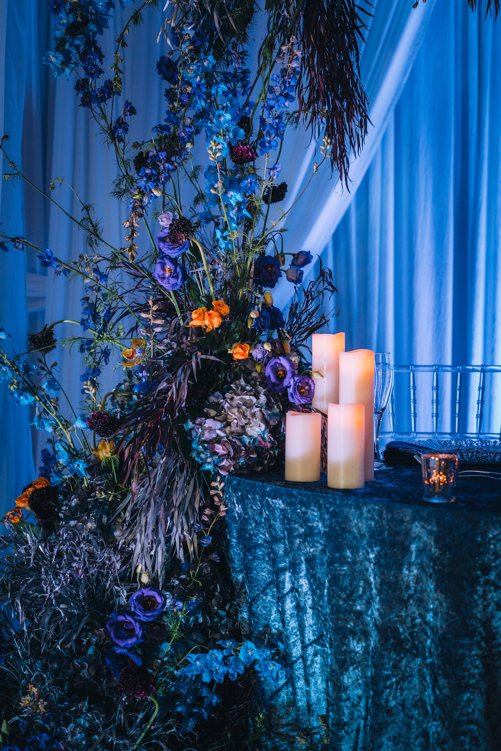Creative Modern Contemporary Dark and Dramatic Wedding Reception Decor, Sweetheart Table with Blue Linen, Candlesticks, Linen Drapery Backdrop and Blue Uplighting, Unique Blue, Purple, Orange, Dark Purple, Floral Arrangement | Tampa Bay Wedding Planner Special Moments Event Planning | Wedding Rentals Gabro Event Services | Styled Shoot